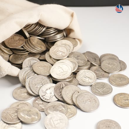 90% Silver bag with silver coins spilling onto white counter surface, Monument Metals logo in top right hand corner