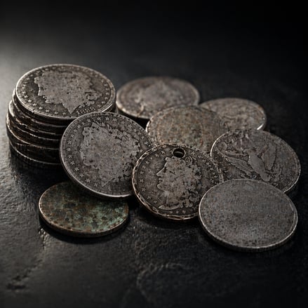 Pile of heavily worn and damaged cull silver coins including holed Morgan dollars and corroded pieces on a dark surface