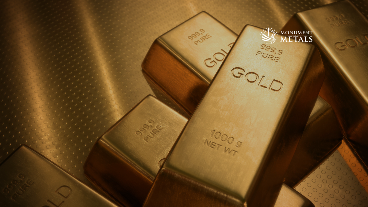 Close-up image of stacked 999.9 pure gold bars, including a 1000g bar, displayed on a textured gold surface with the Monument Metals logo in the upper right.
