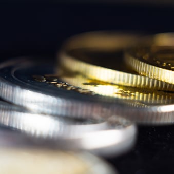 Macro close-up of stacked gold and silver bullion coins with shallow depth of field, highlighting detailed edges and reflective surfaces against a dark background.