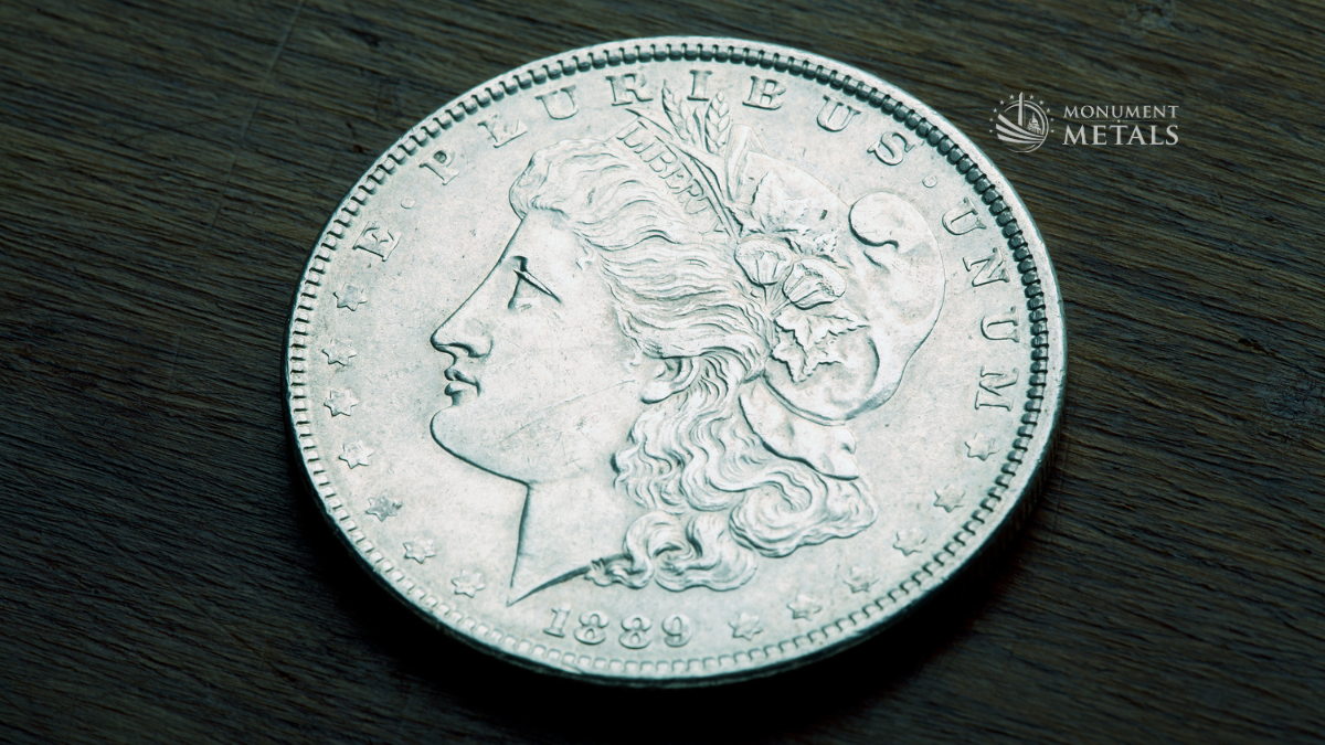 1889 Morgan Silver Dollar obverse close-up on dark wood surface with strong detail and natural toning, Monument Metals logo visible