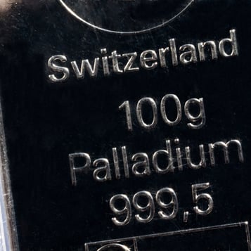 Close-up of a Swiss palladium bar showing “Switzerland,” “100 g,” and “Palladium 999.5” stamped on a reflective surface.