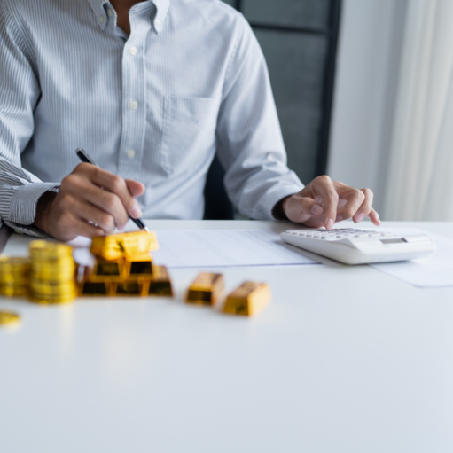Buyer using a calculator to track average cost beside stacks of gold coins and gold bars