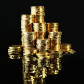 Tall stacks of gold coins arranged on a glossy black reflective surface, creating mirrored reflections and emphasizing wealth, gold accumulation, and bullion stacking.