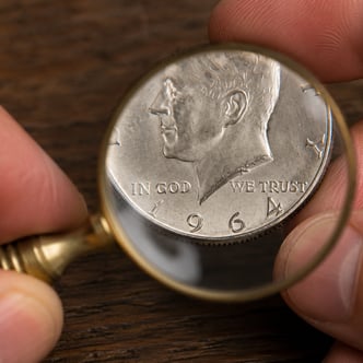 1964 Kennedy half dollar examined under magnifying glass showing date and portrait for junk silver identification