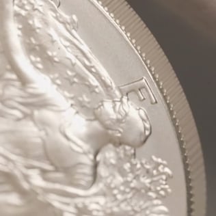Extreme close-up of a silver bullion coin featuring Lady Liberty in profile. The image highlights the coin’s frosted finish, intricate engraving details, and finely reeded edge, with a shallow depth of field creating a soft, blurred background. The composition emphasizes the craftsmanship and texture of the silver coin.