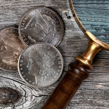 Morgan dollars and magnifying glass on wooden surface