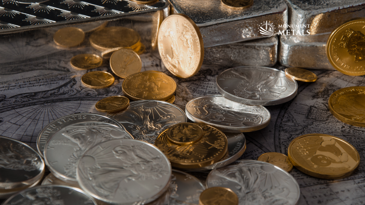 Gold and silver bullion coins and silver bars scattered on a vintage world map, including American Gold Eagles and American Silver Eagles, with the Monument Metals logo in the upper right corner
