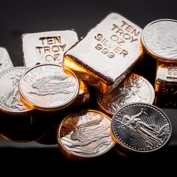 Close-up of .999 fine silver bullion including 10 troy ounce bars and American Silver Eagle coins arranged on a dark reflective surface with warm lighting.