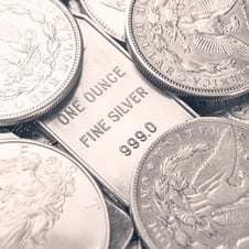 One-ounce 999 fine silver bar surrounded by silver coins, including detailed close-up views of classic U.S. coin designs.