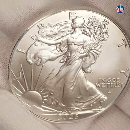 American Silver Eagle resting in white glove with Monument Metals logo in top right hand corner 