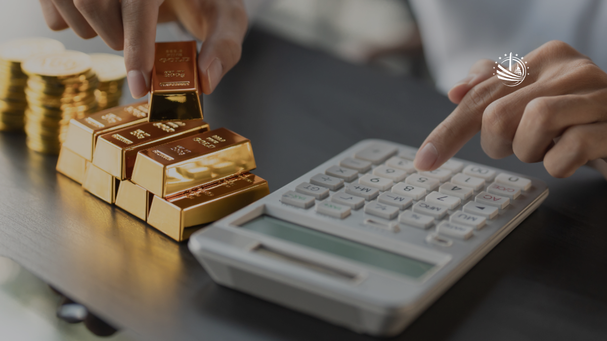 Hands stacking gold bars beside a calculator as someone presses the keys, illustrating the process of calculating the value of physical gold based on weight and price.