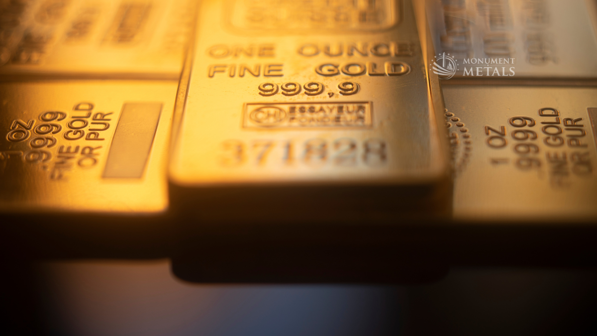 Stacked 24k gold bars stamped one ounce fine gold 999.9 with Monument Metals logo and warm reflective lighting